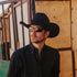 Man wearing a black cowboy hat and sunglasses against a rustic background