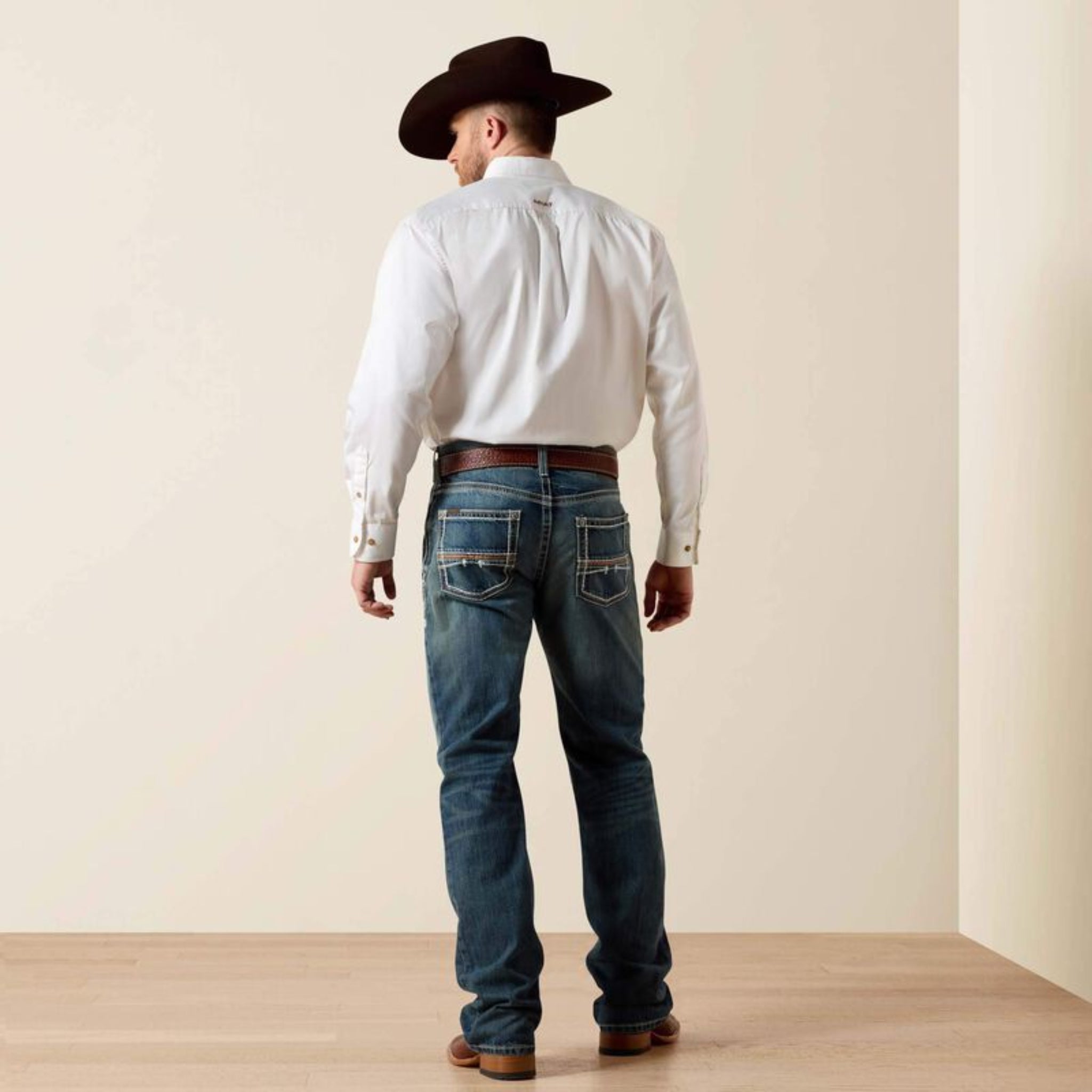 Man wearing a white shirt, blue jeans, and a cowboy hat 