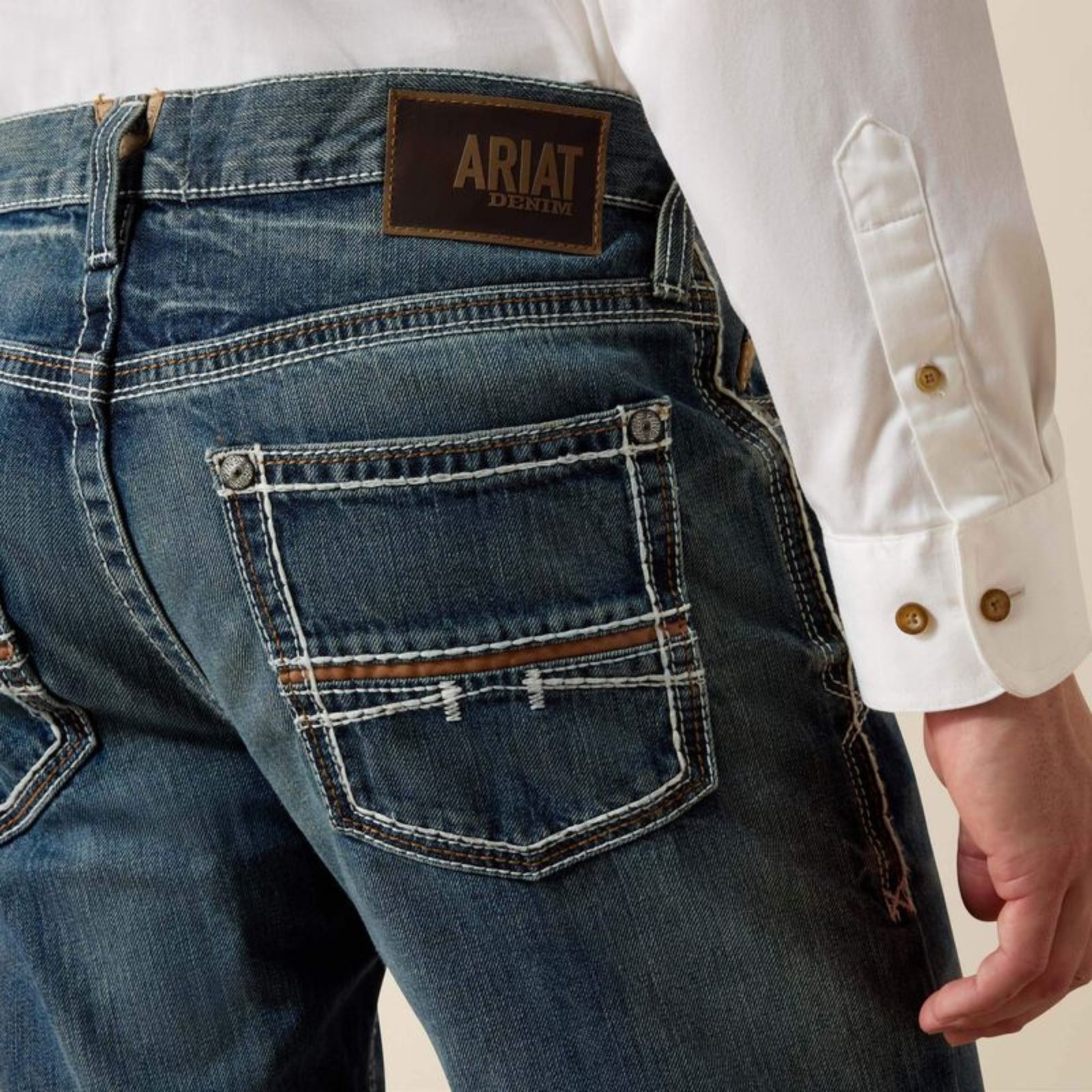 Close-up of blue jeans with Ariat logo and a white shirt.