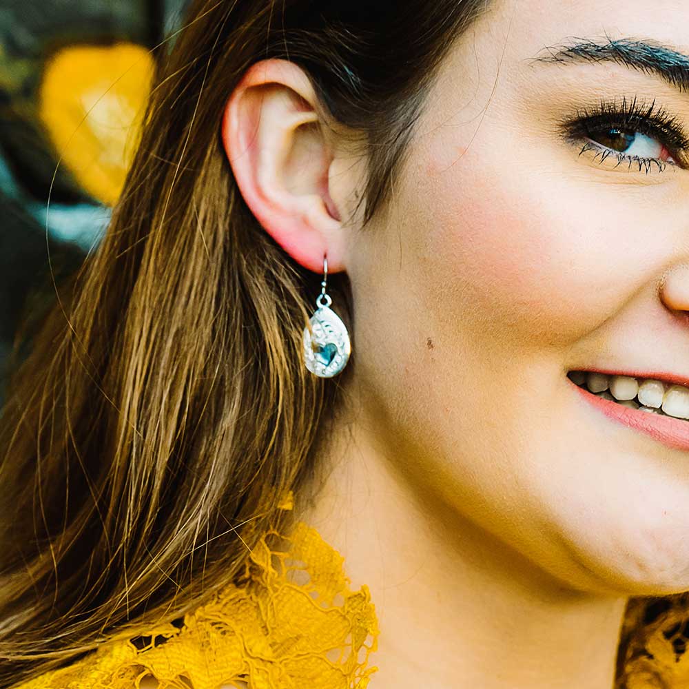 Close-up of a woman wearing a silver earring with blue gemstone, smiling outdoors.