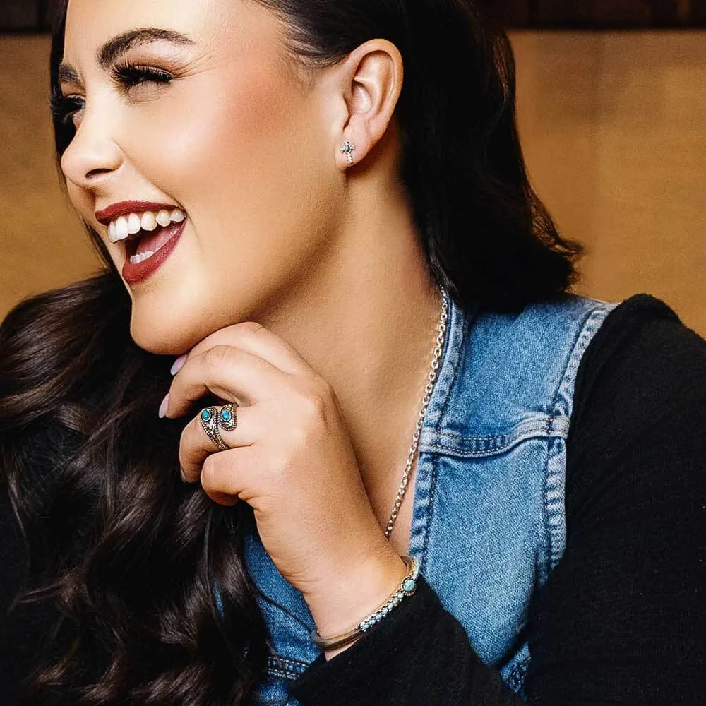 Woman with a smile, wearing a denim vest and cross earings 