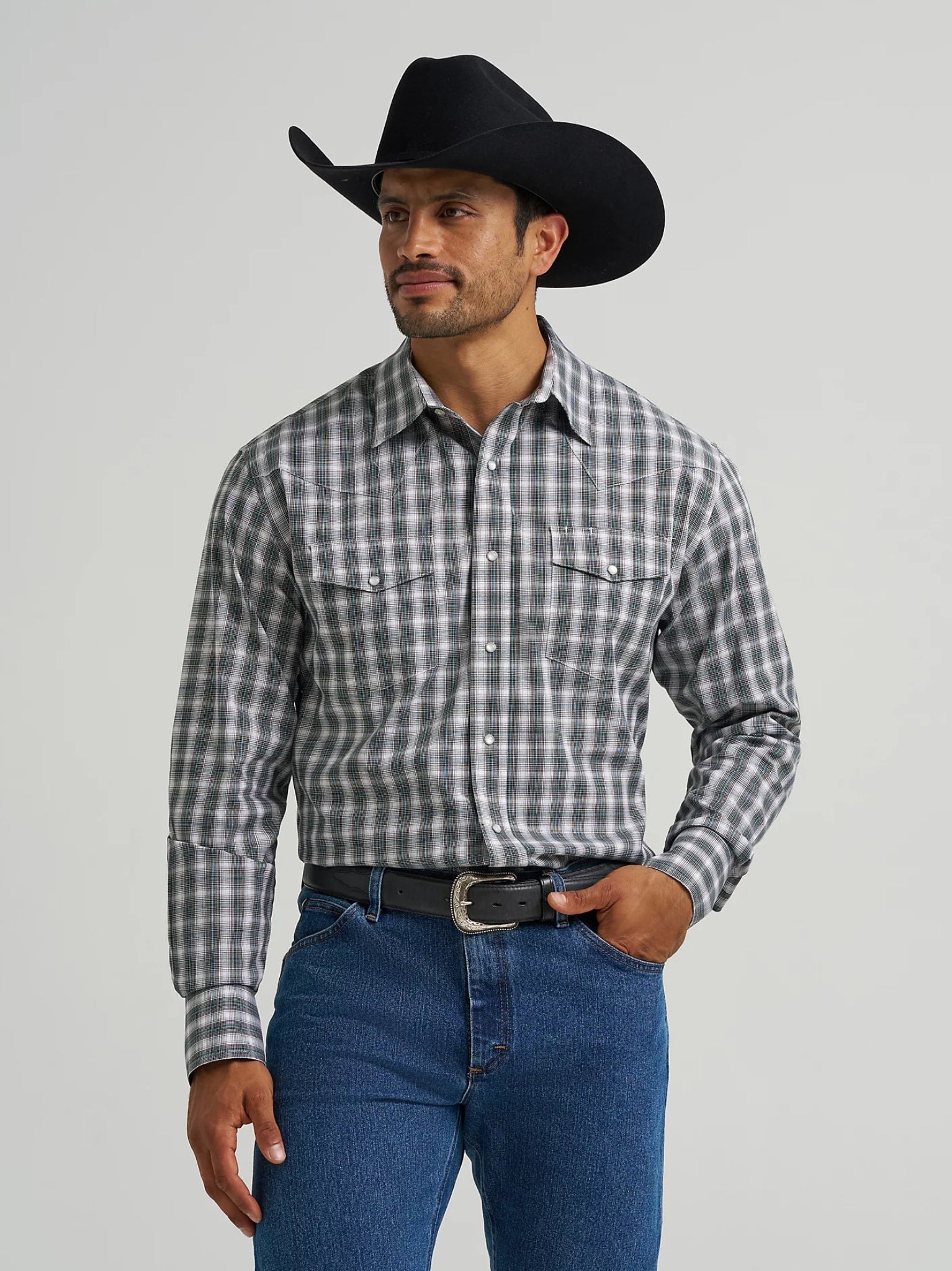 Man wearing a black cowboy hat, plaid shirt, and blue jeans on a gray background