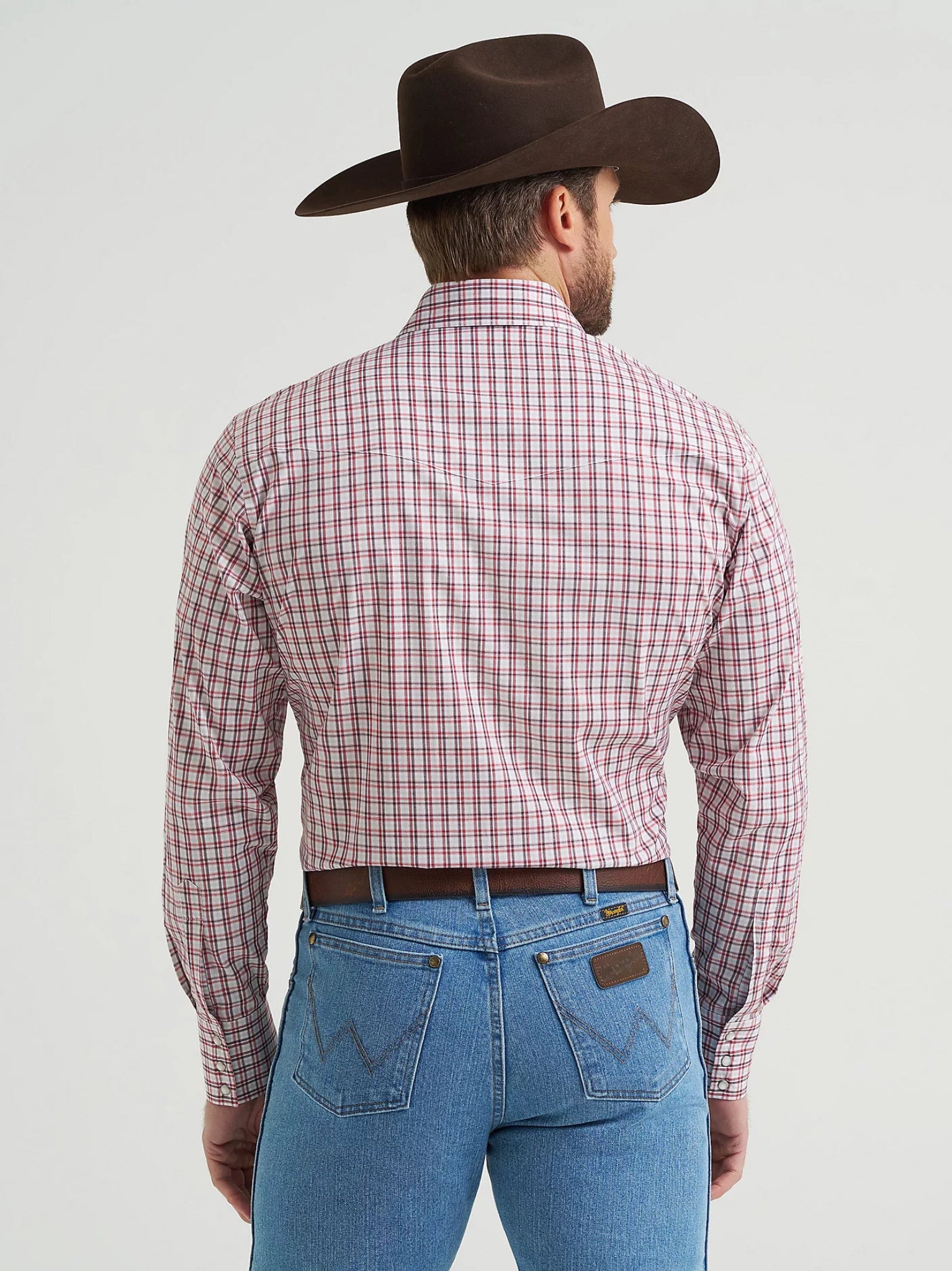 Man wearing a red plaid shirt, blue jeans, and a brown cowboy hat