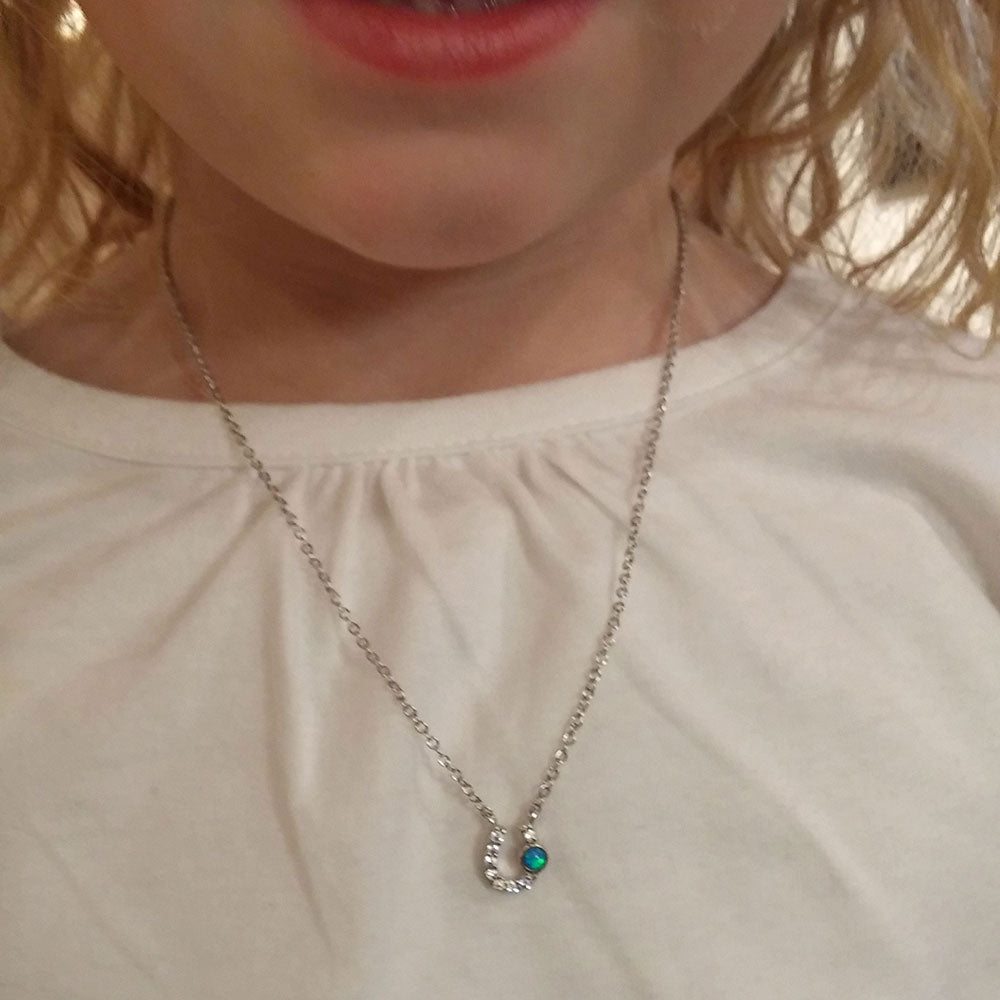 Necklace with a small green gemstone worn by a person on a plain background