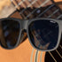Black sunglasses with 'BEX' logo on an acoustic guitar