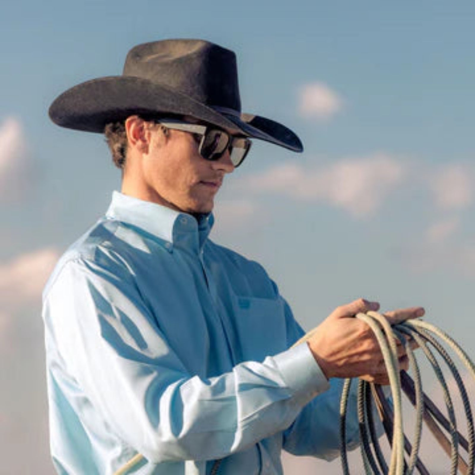 Man wearing a cowboy hat and sunglasses, holding a rope 