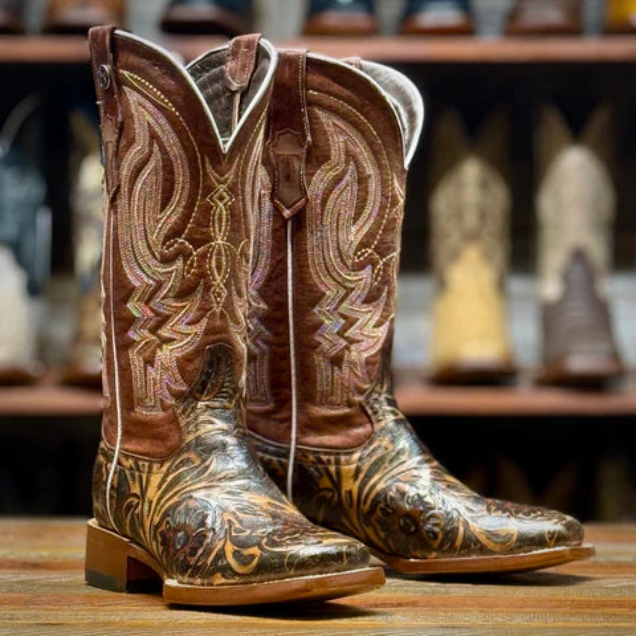 Pair of brown and light brown cowboy boots with jungle patterns on a wooden surface.
