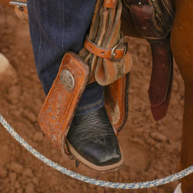 Close-up of a cowboy boot in a stirrup on a horse, with a blurred background.