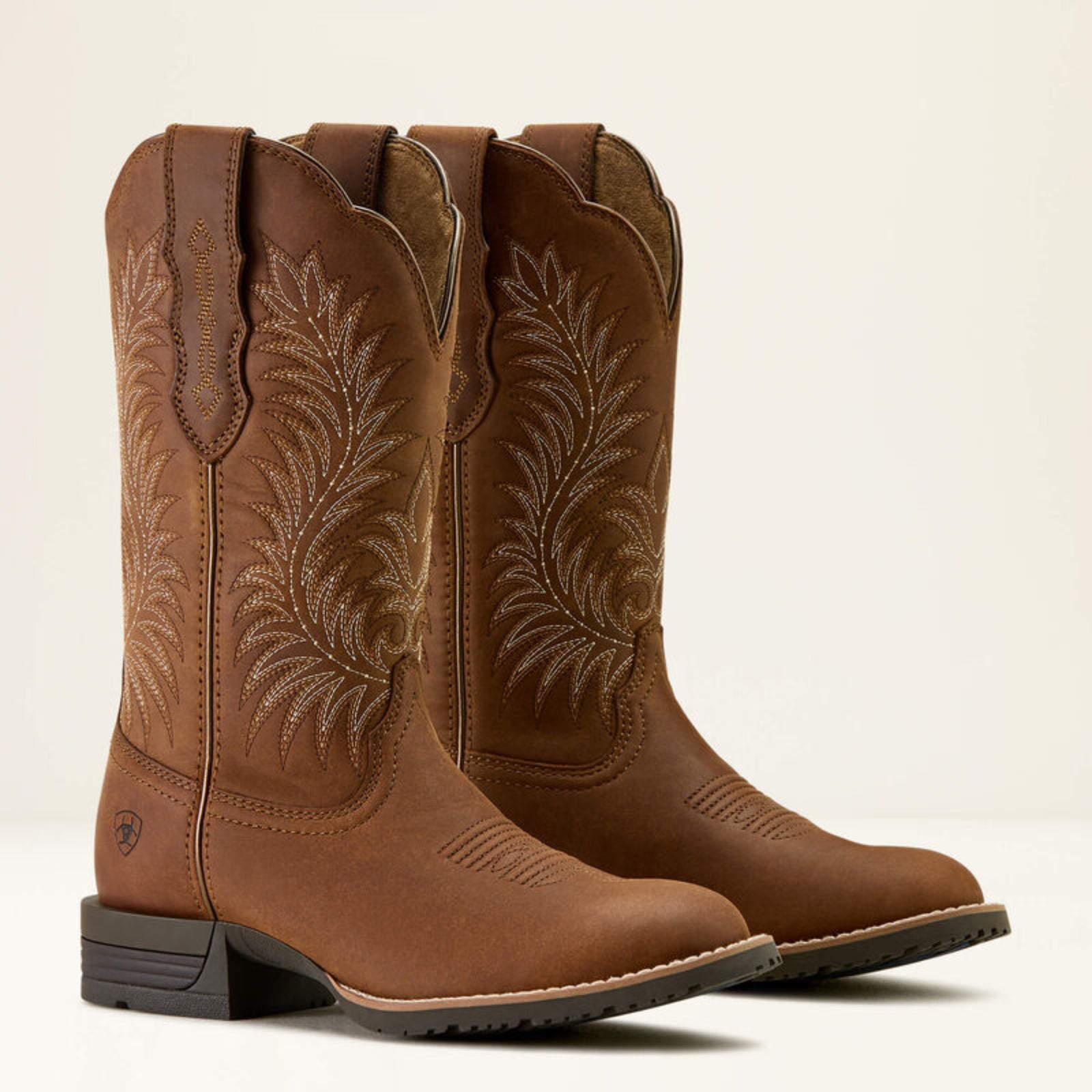 Pair of brown cowboy boots with intricate stitching on a beige background