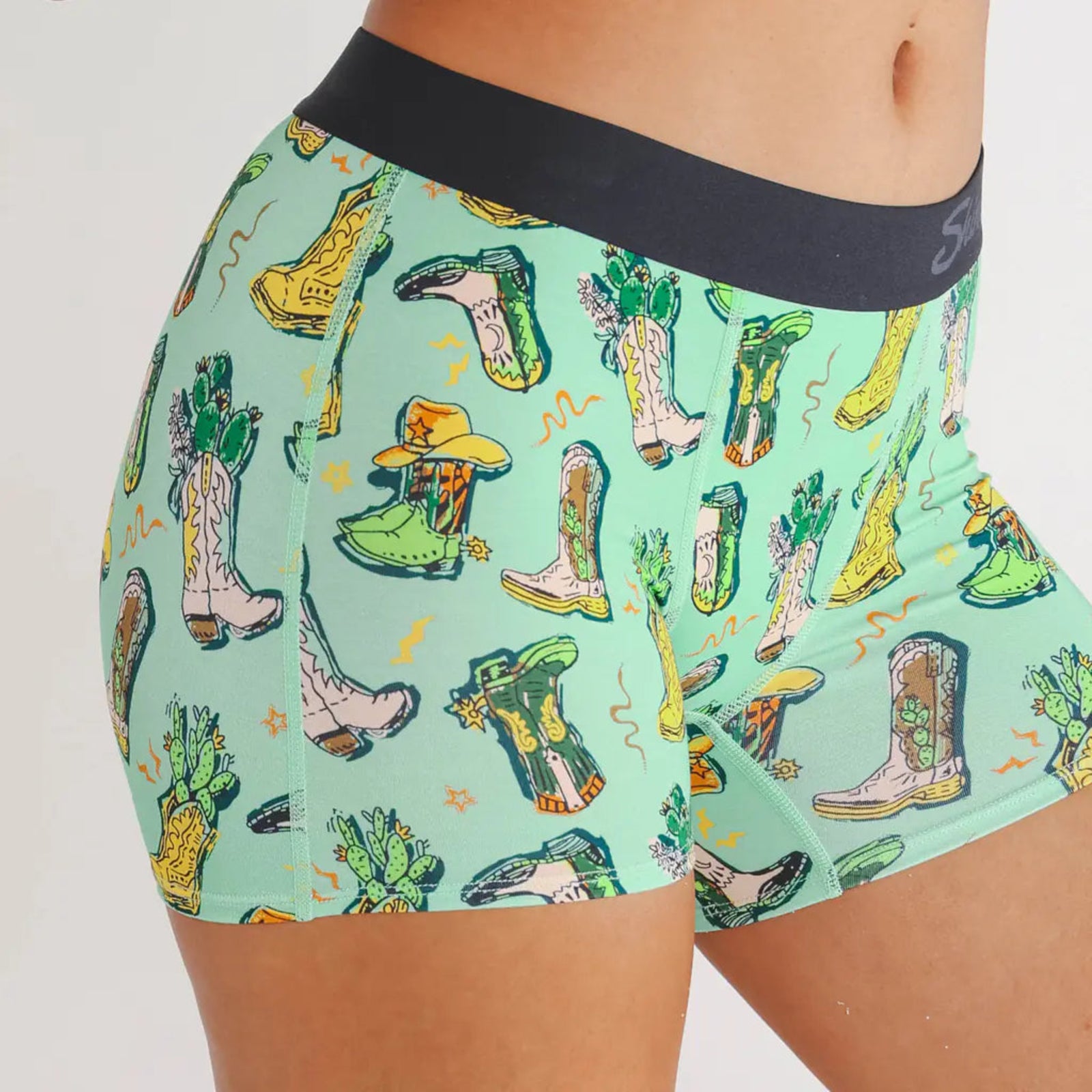 Shorts with cowboy boot and cactus pattern on a light green background